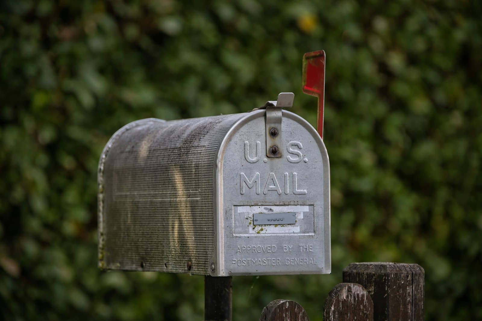 Classic post-mounted mailbox with the flag up in front of a hedge