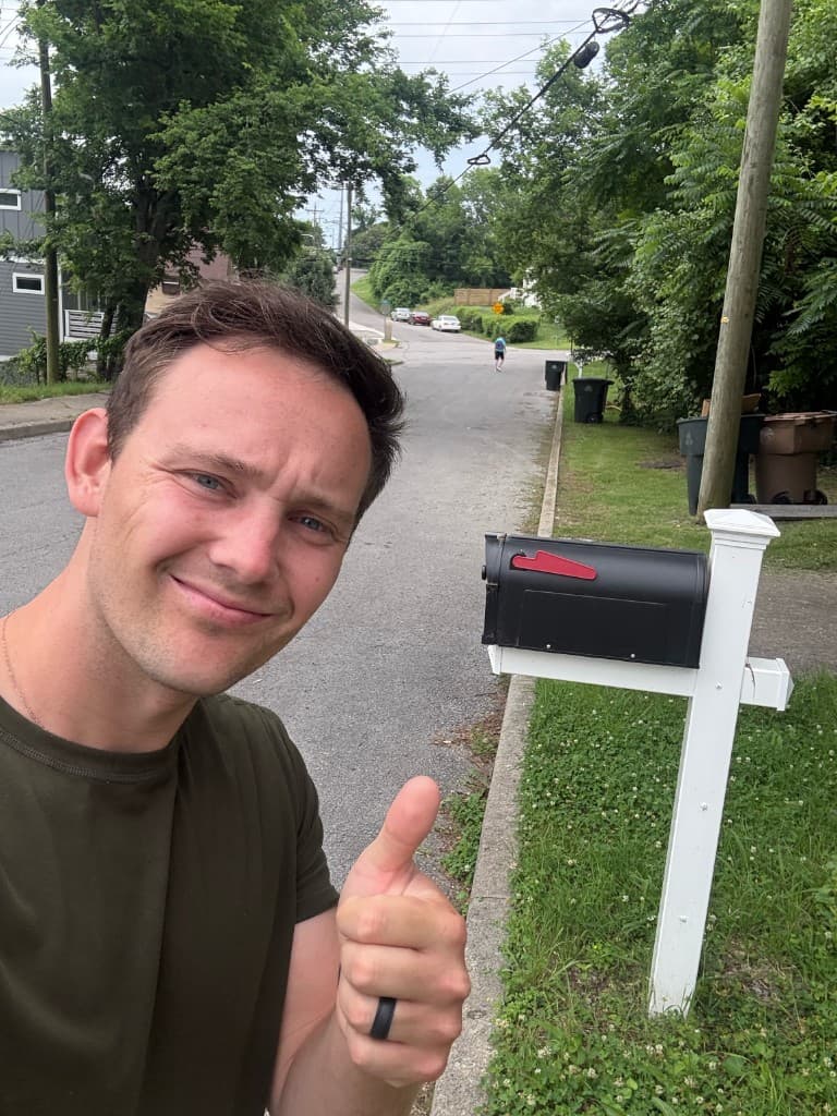 Mailbox Bros team member giving a thumbs up beside a black mailbox on a white post