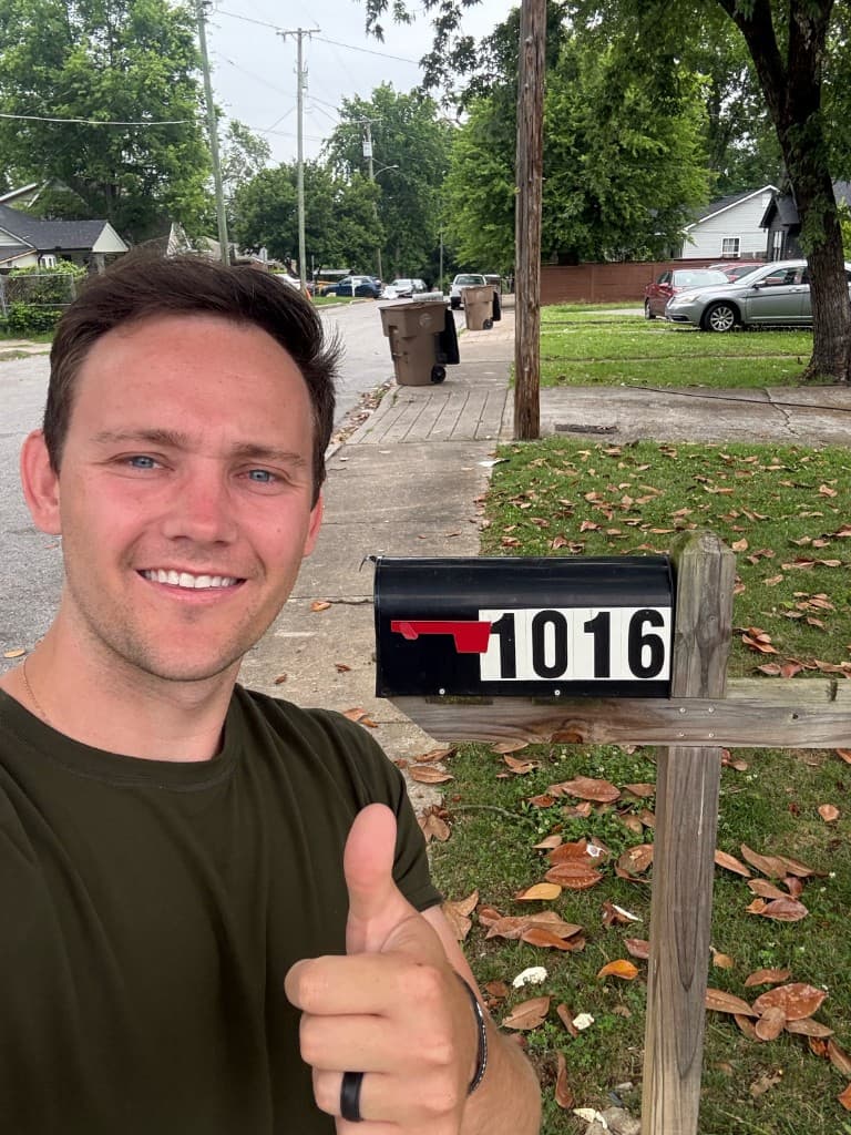 Mailbox Bros team member taking a thumbs-up selfie beside a numbered black mailbox